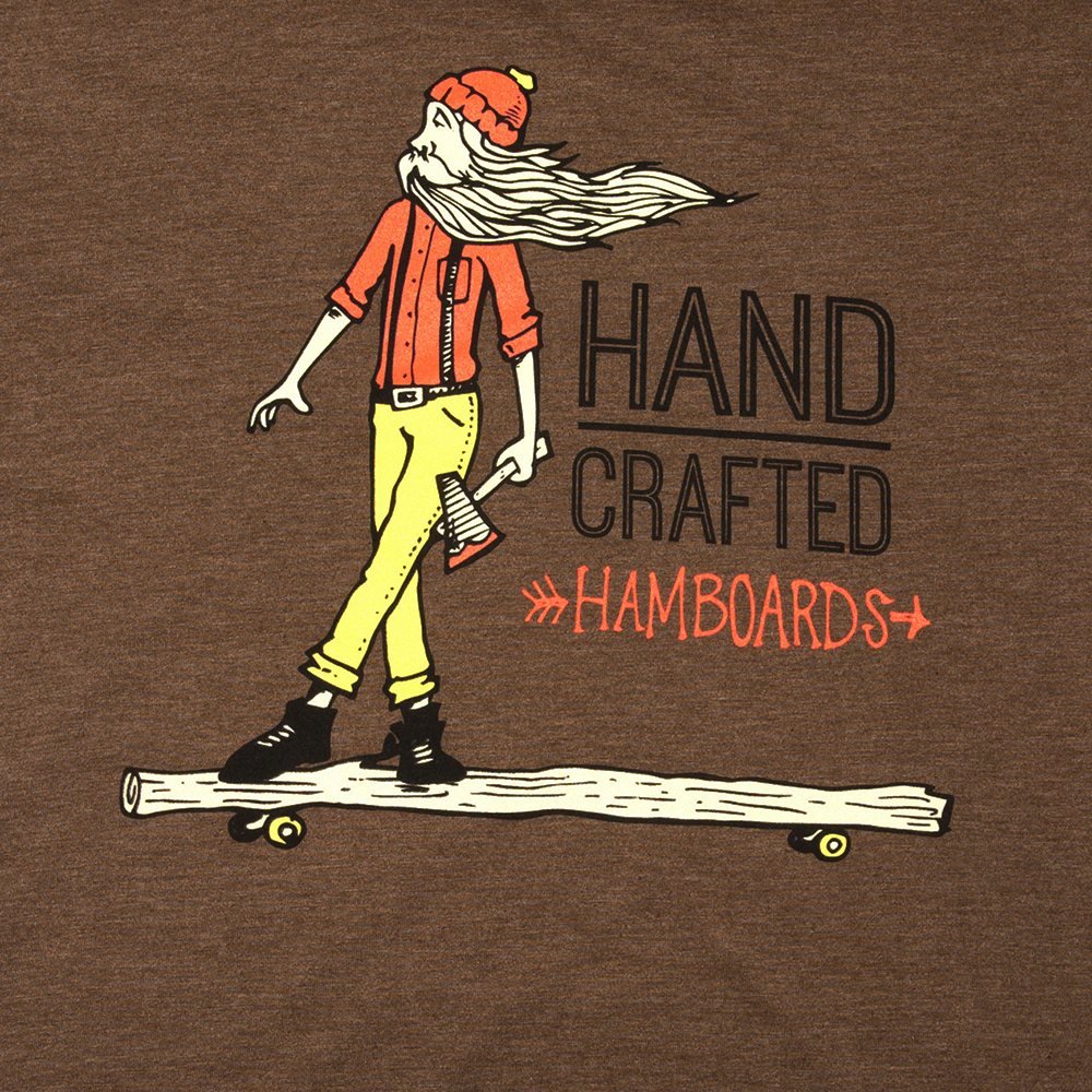 Close-up of the Hand Crafted print on a brown T-shirt: a bearded lumberjack with an axe standing on a log fitted with skateboard wheels